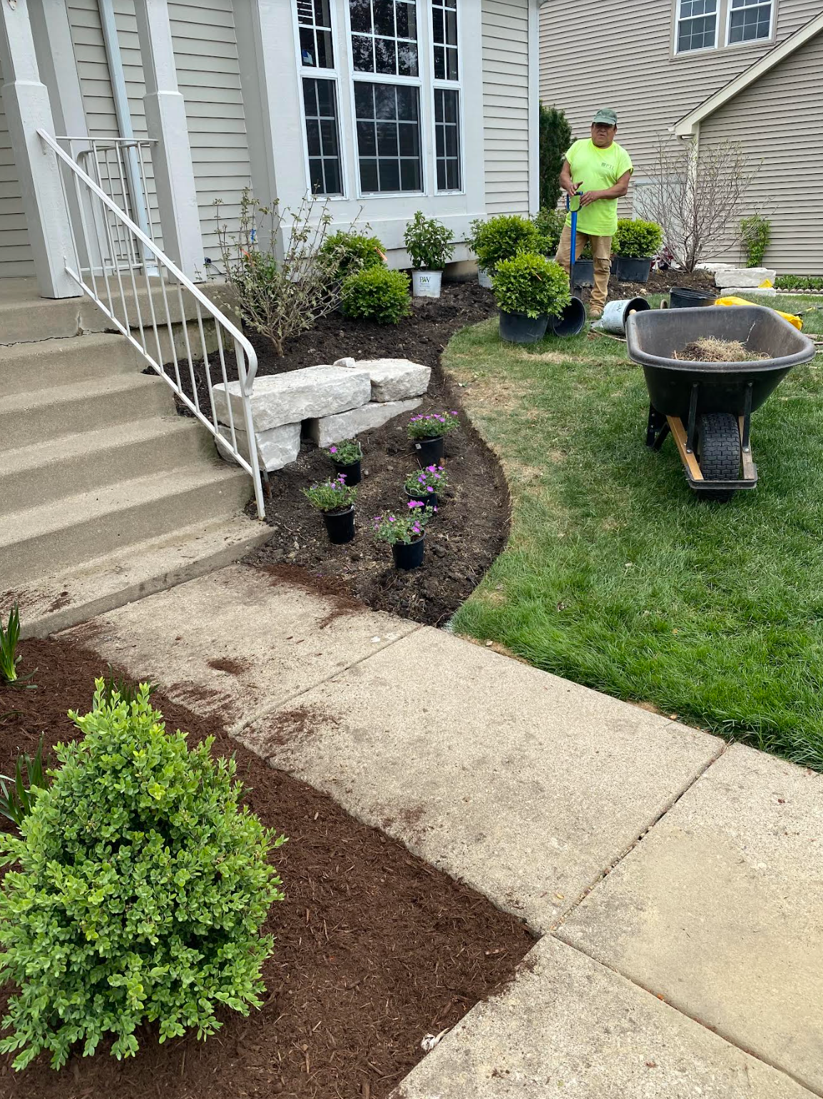 A man is standing next to a wheelbarrow in front of a house.