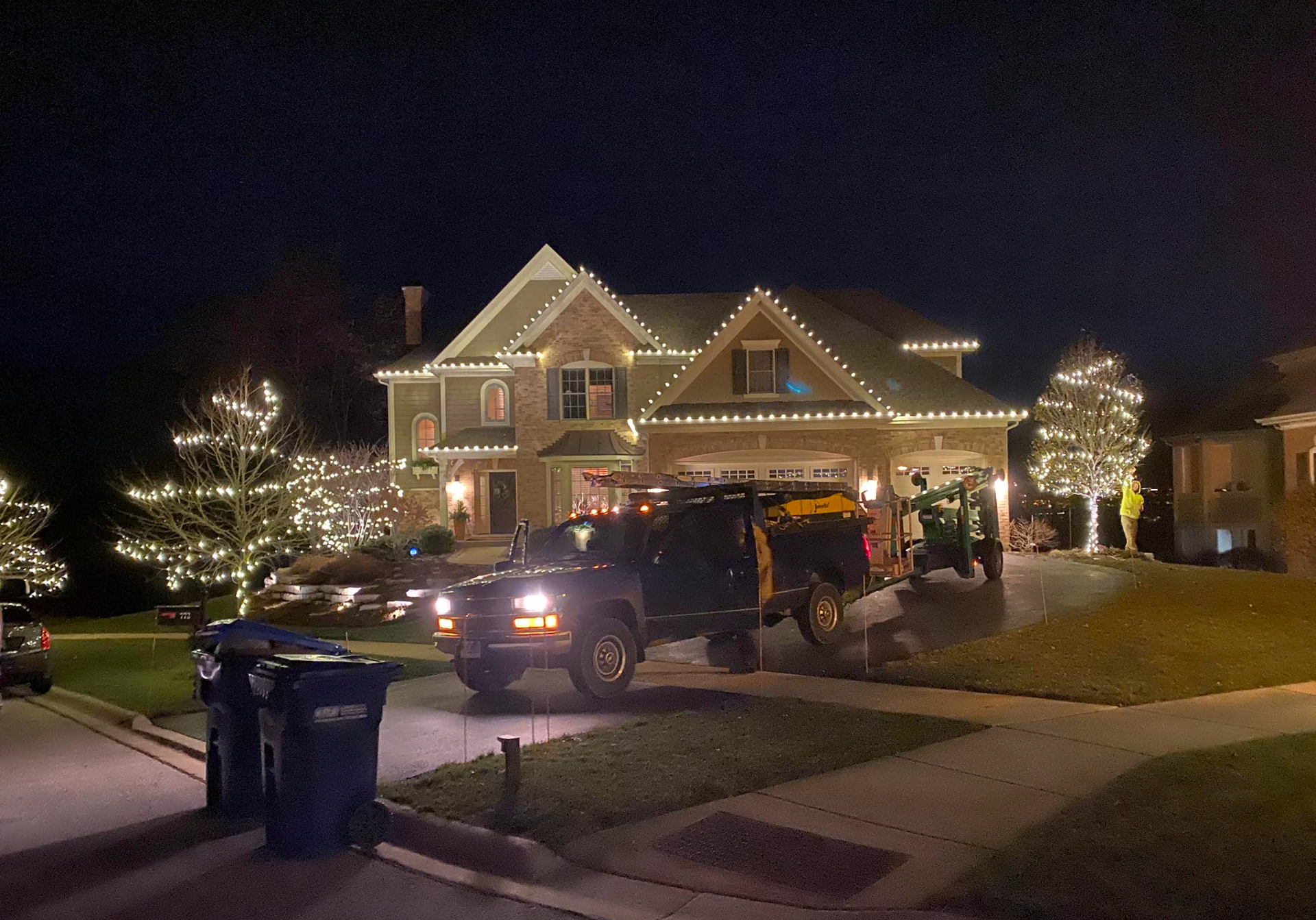 House decorated with Christmas lights at night, truck in driveway.