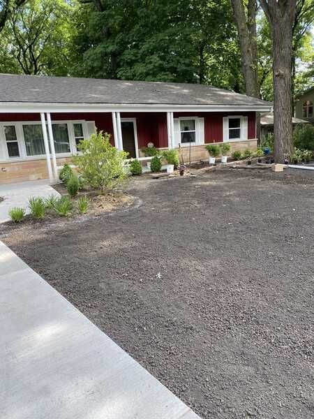 Red-sided house with white trim, new landscaping, and a gravel yard. Gray sidewalk leads to the house.