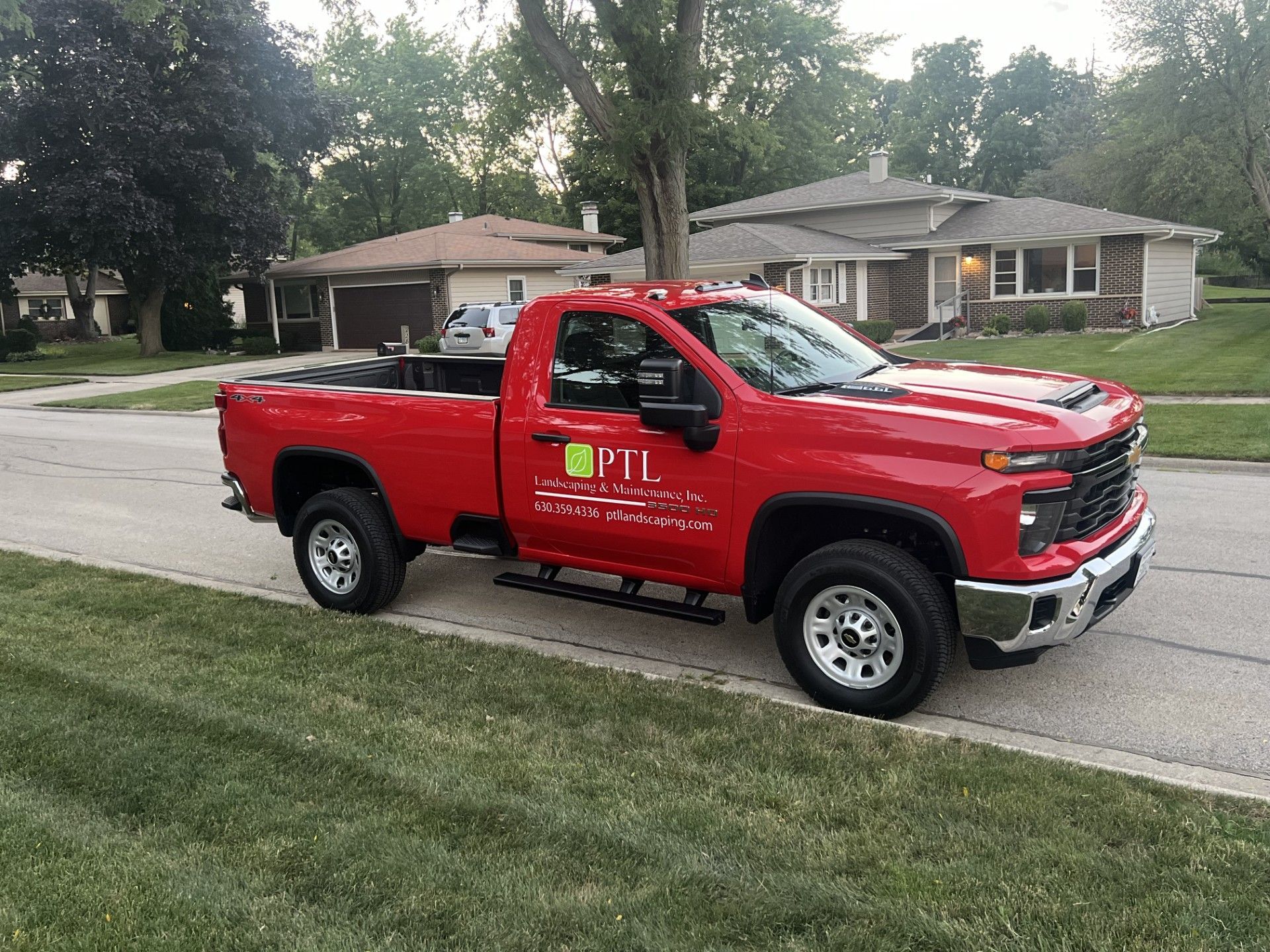 Red pickup truck parked on grass in a residential area. Truck has company logo on the door.