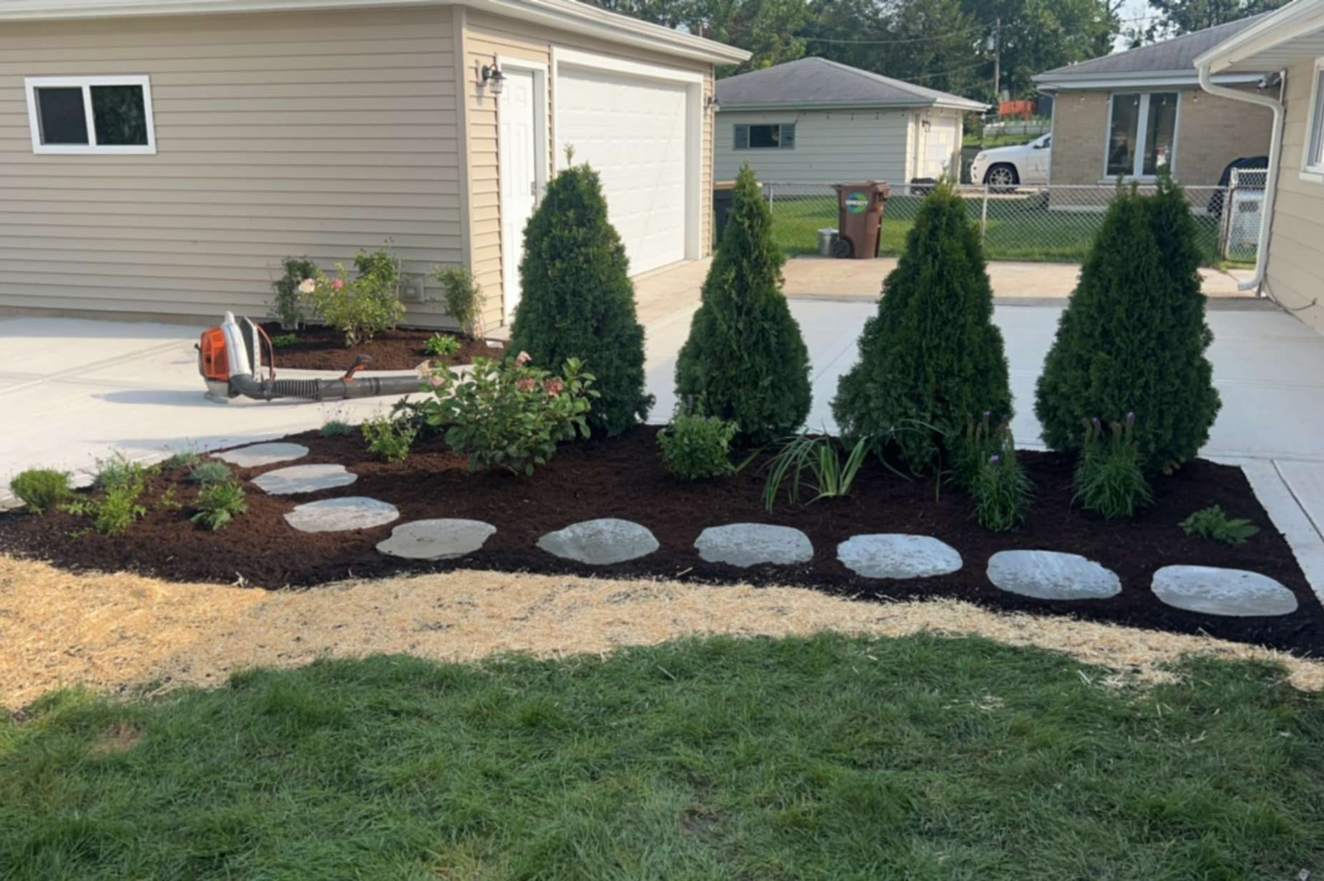 Landscaped yard with stepping stones, evergreens, and fresh mulch near a garage.
