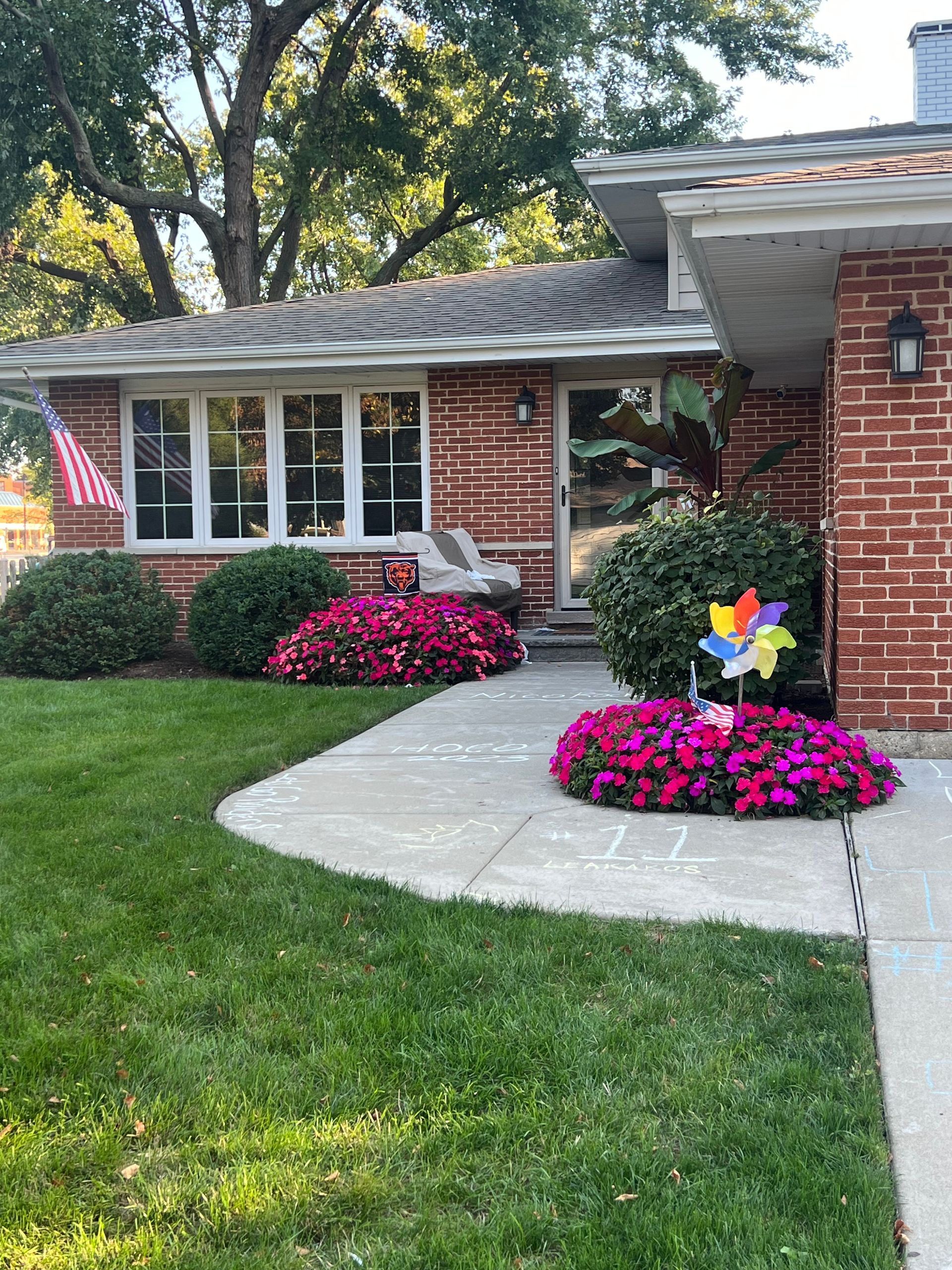 Red brick house with a well-manicured lawn, vibrant pink flowers, and a colorful pinwheel.