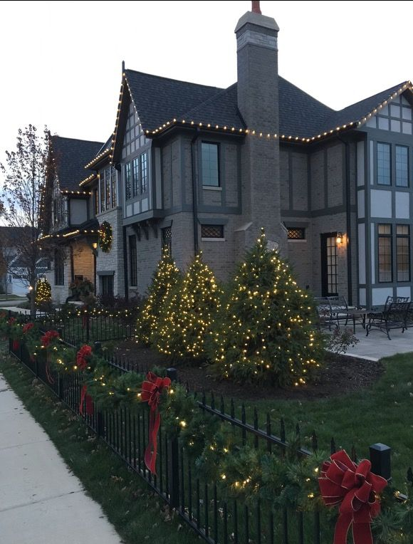 House decorated for Christmas with lights on the trees, garland on a fence, and red bows.