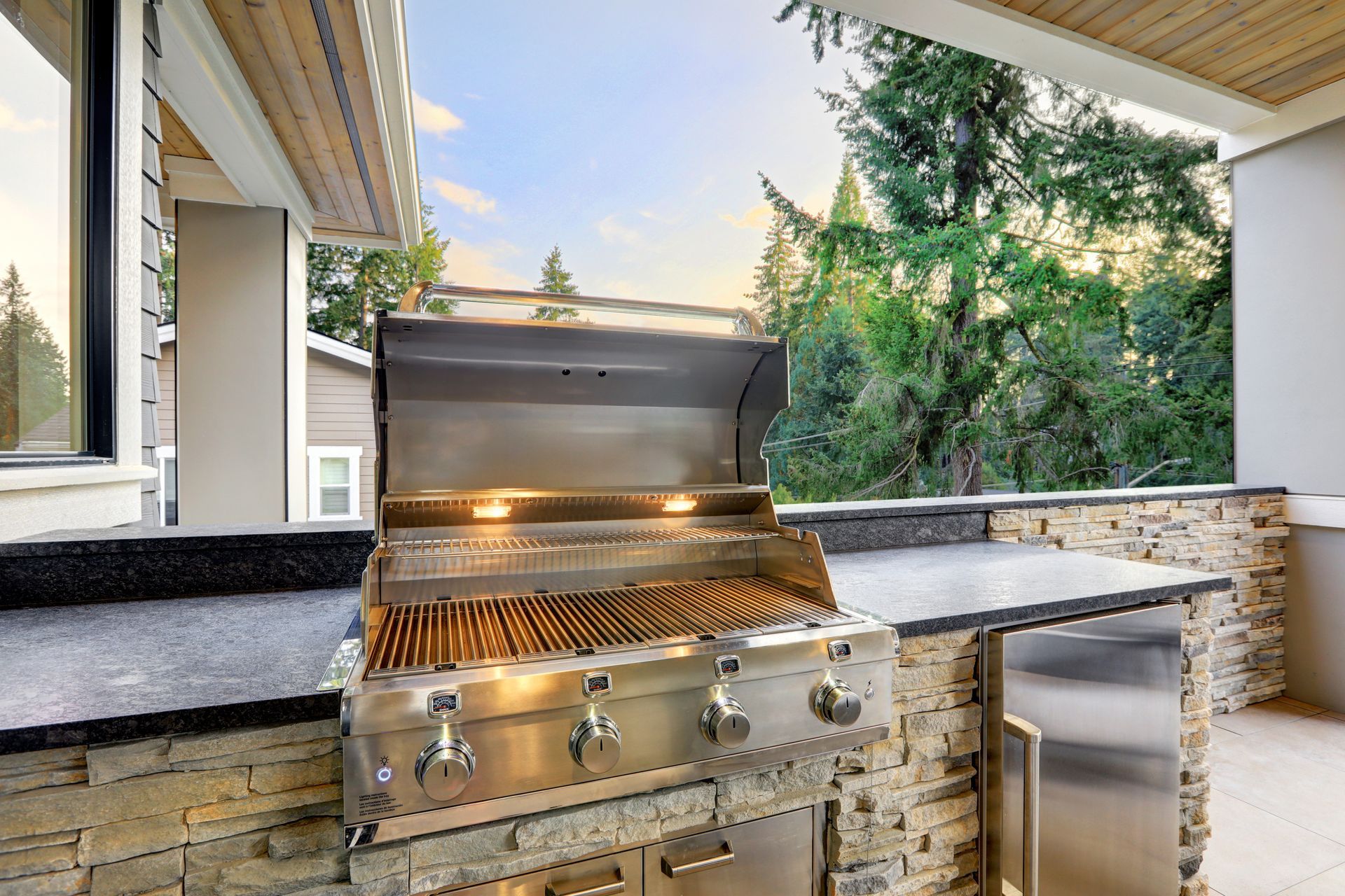 Stainless steel grill on a stone counter with a built-in fridge, outdoors.