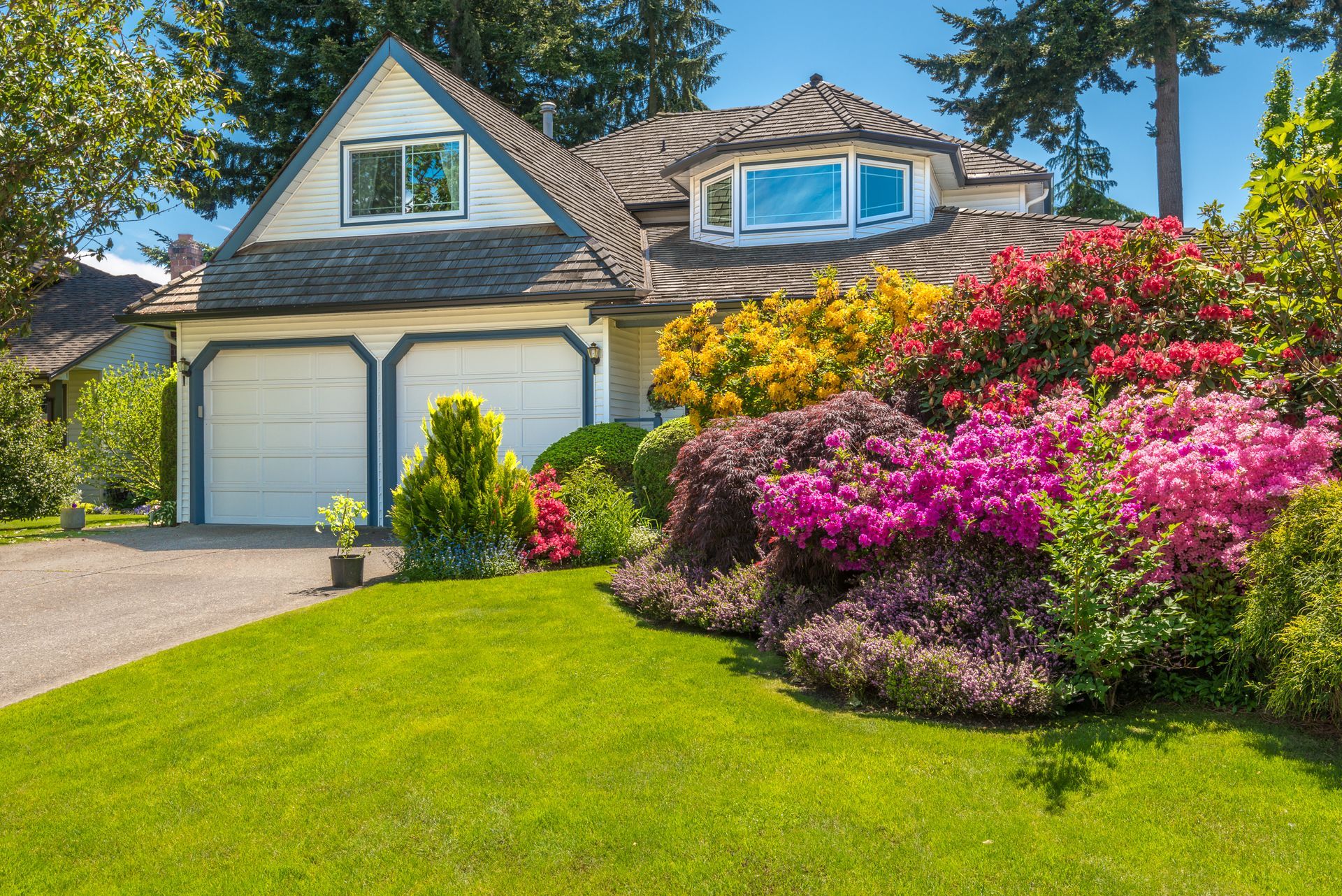 House with white garage doors and colorful blooming flowers in a lush green garden.