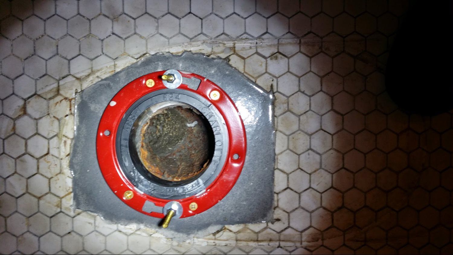 A close up of a toilet flange on a tiled floor.