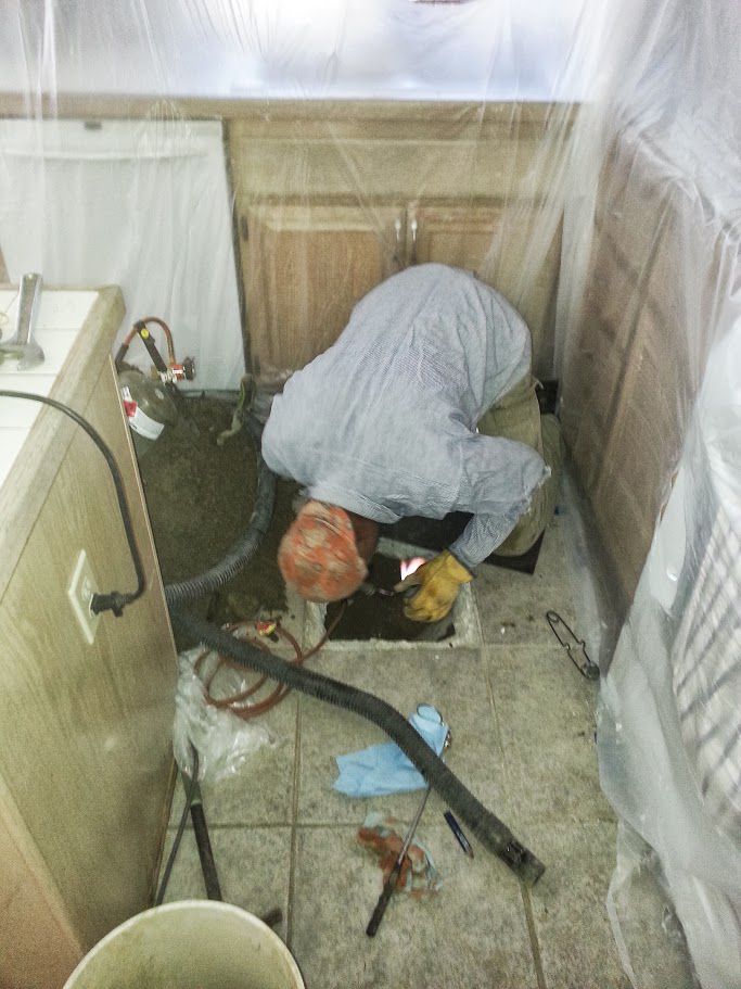 A man is kneeling down in a kitchen with a vacuum cleaner.