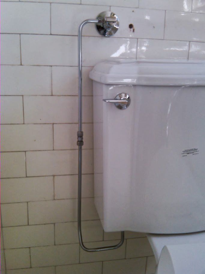 A toilet with a pipe attached to it in a bathroom.