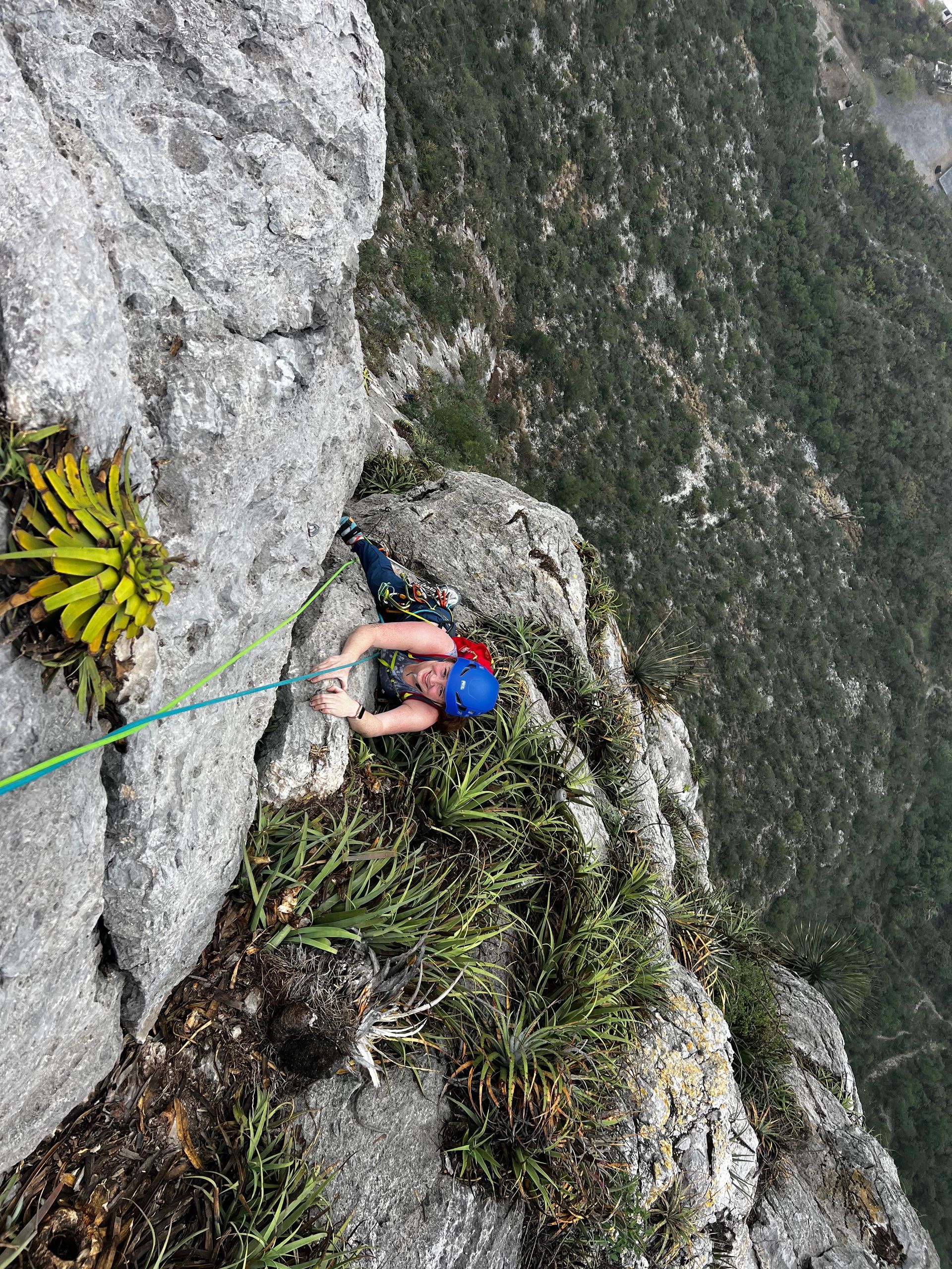 A person is climbing up a rocky cliff with a rope.