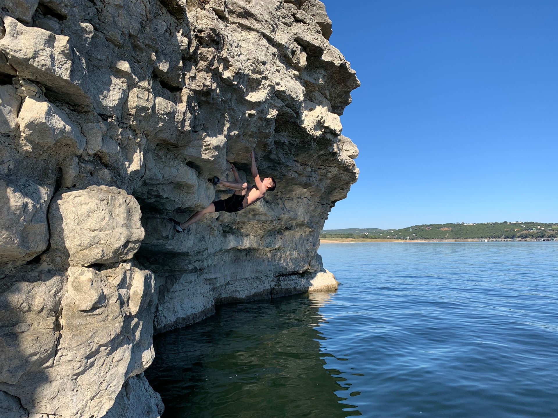 A person is climbing a rock wall next to a body of water.