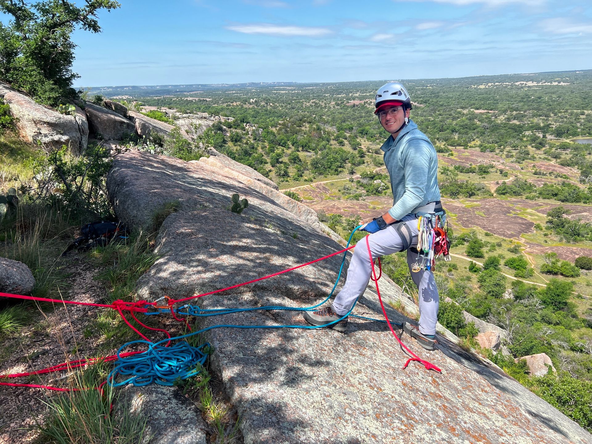 A climber in a helmet at the top of a granite slab at Enchanted Rock, managing the ropes