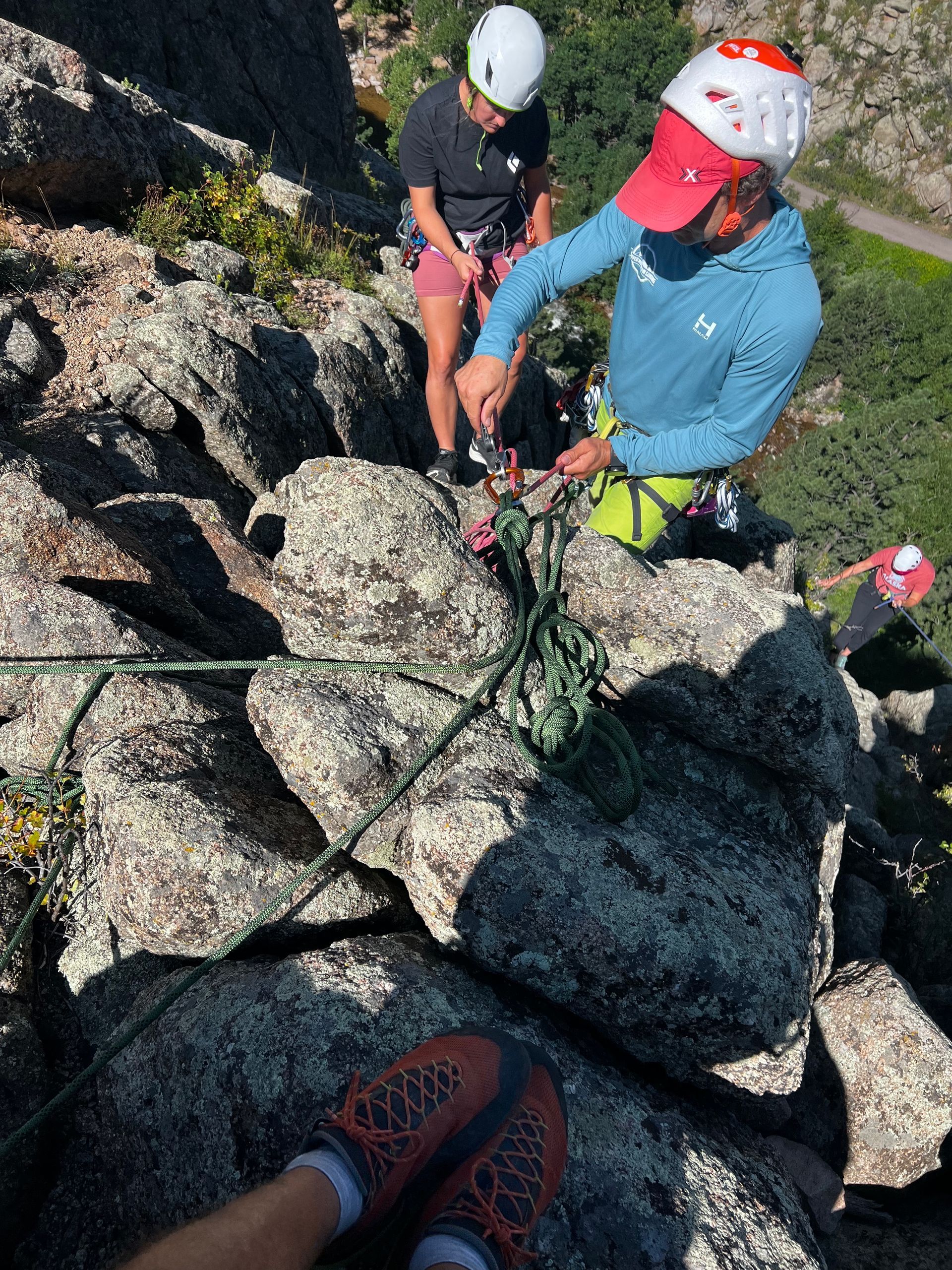 Rock climbers at a granite outcrop: one climbing, two belaying.
