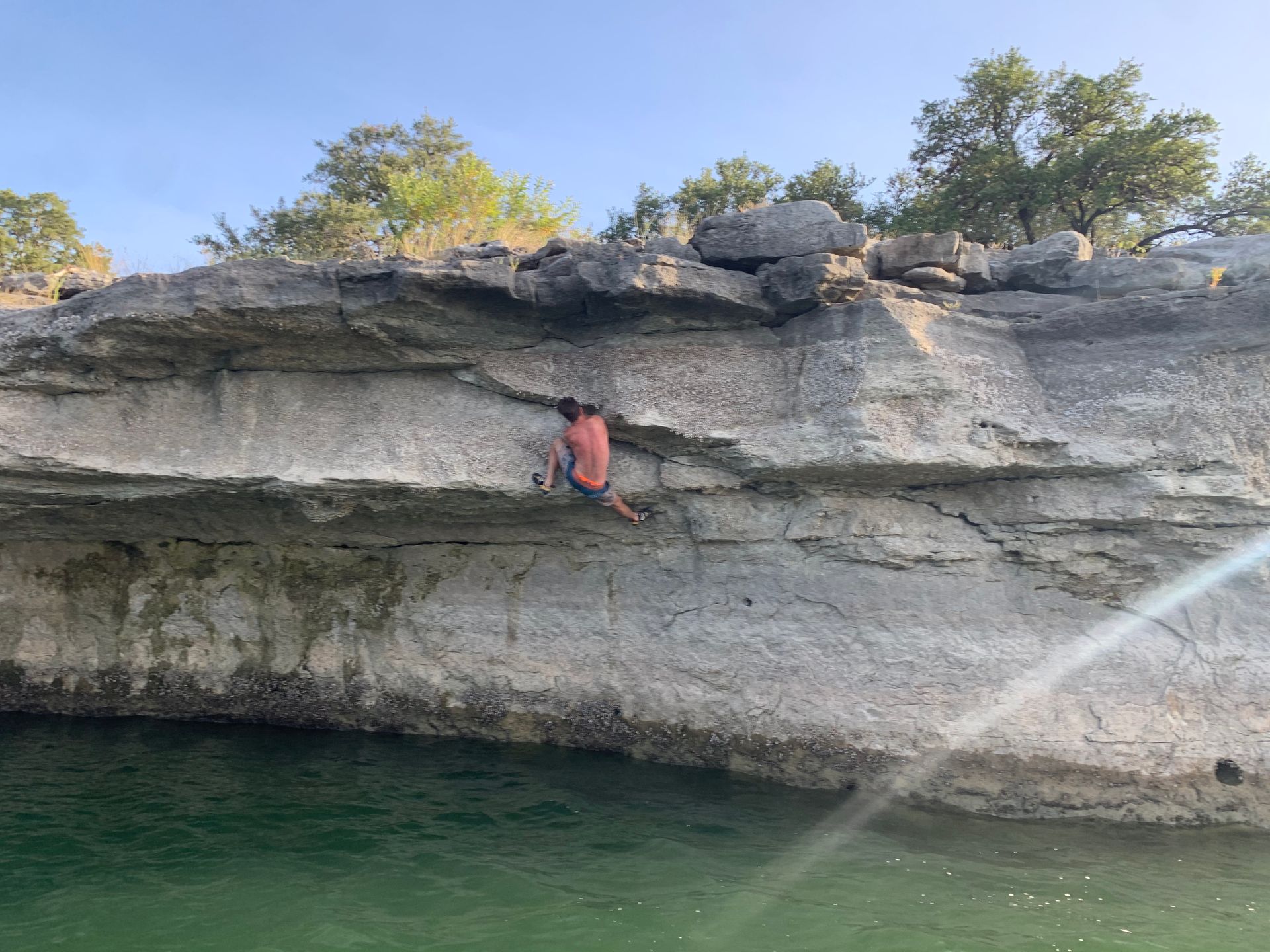 A man is climbing a cliff overlooking a body of water.