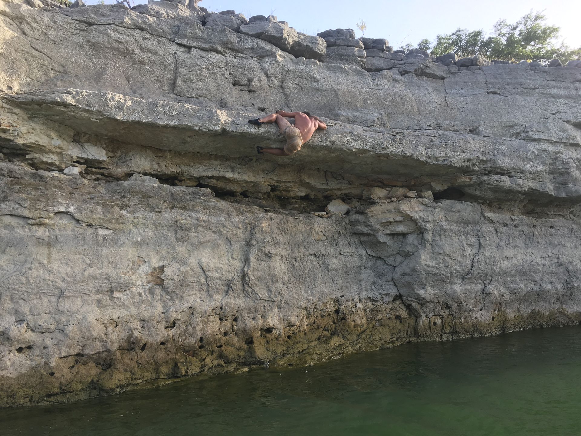 A person is climbing a rock wall next to a body of water.