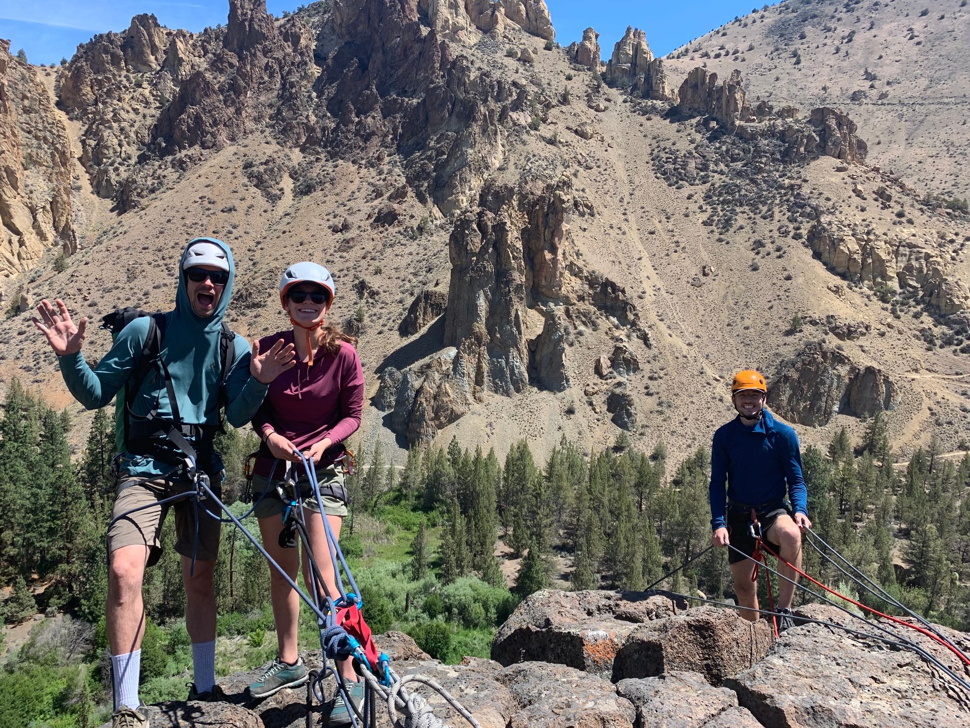 Three friends are standing on top of a rocky mountain