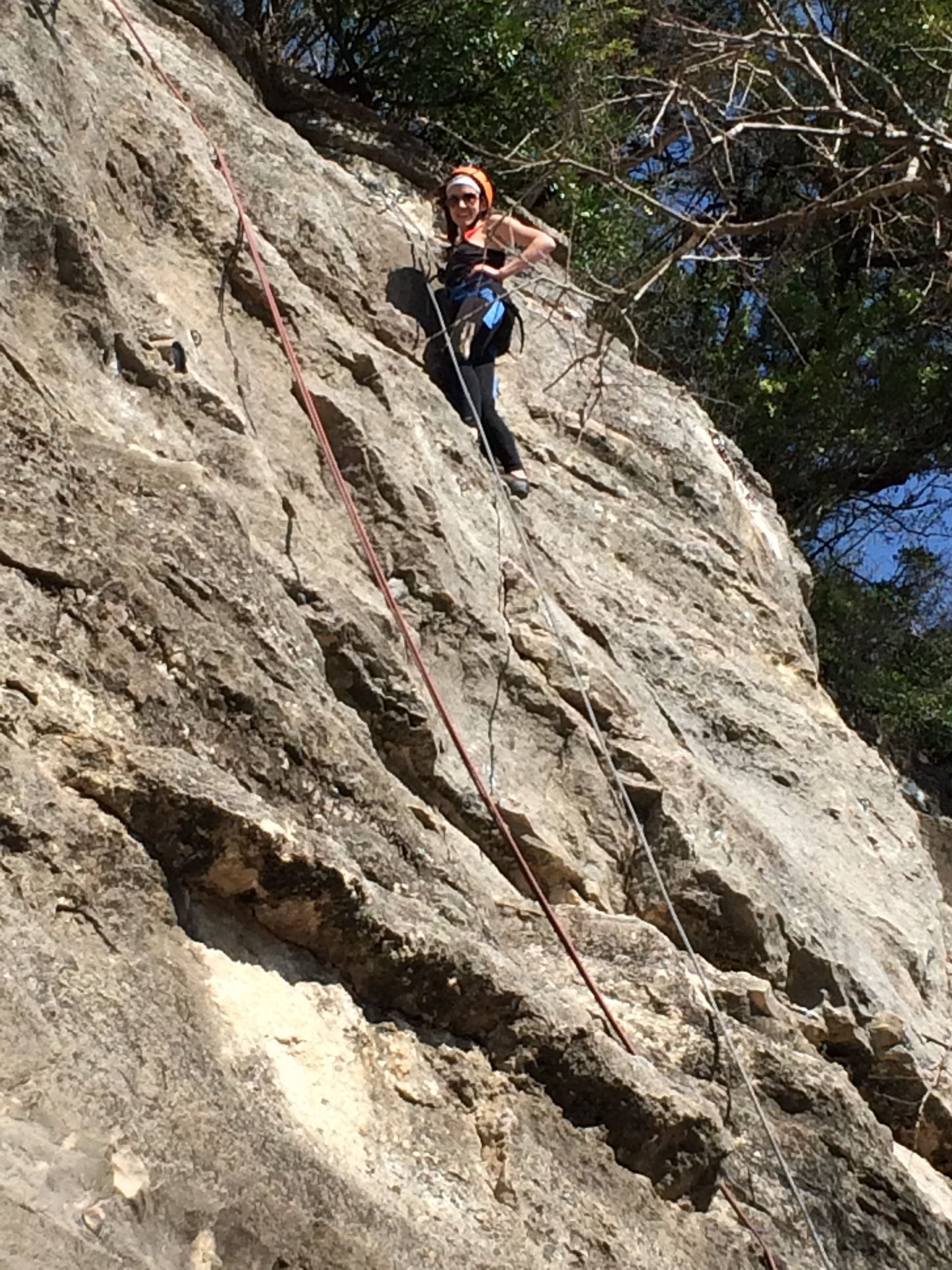 A person rock climbing on a textured, light-colored cliff, secured by a rope.