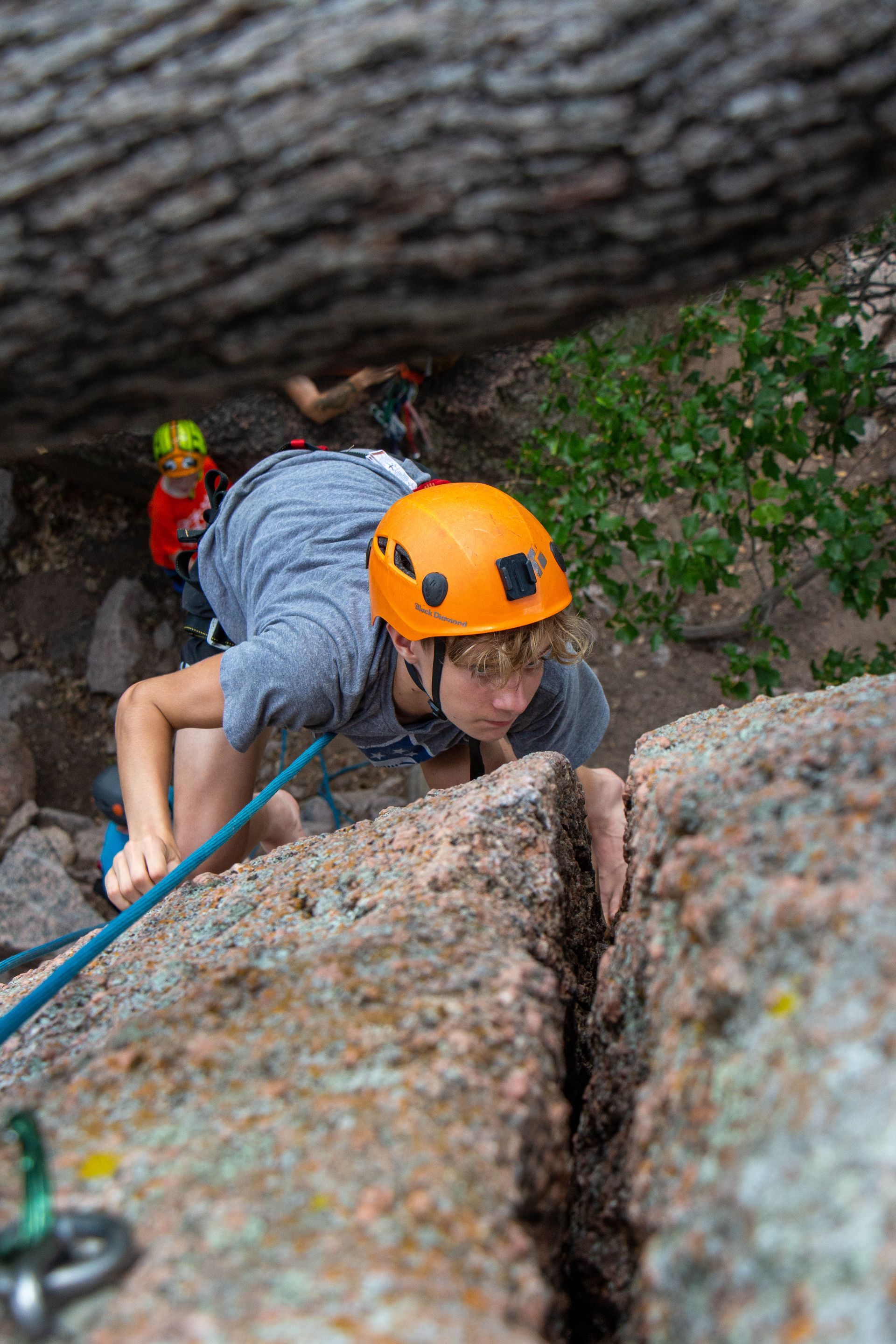A young boy wearing an orange helmet is climbing a rock wall.