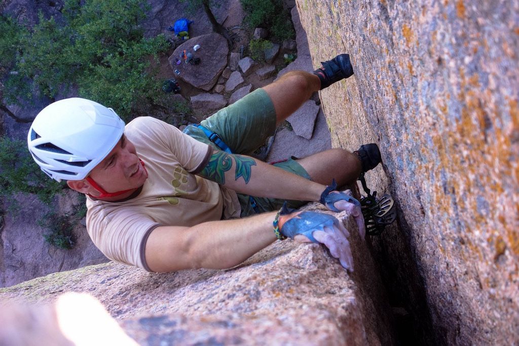 A man wearing a helmet and gloves is climbing a rock wall.