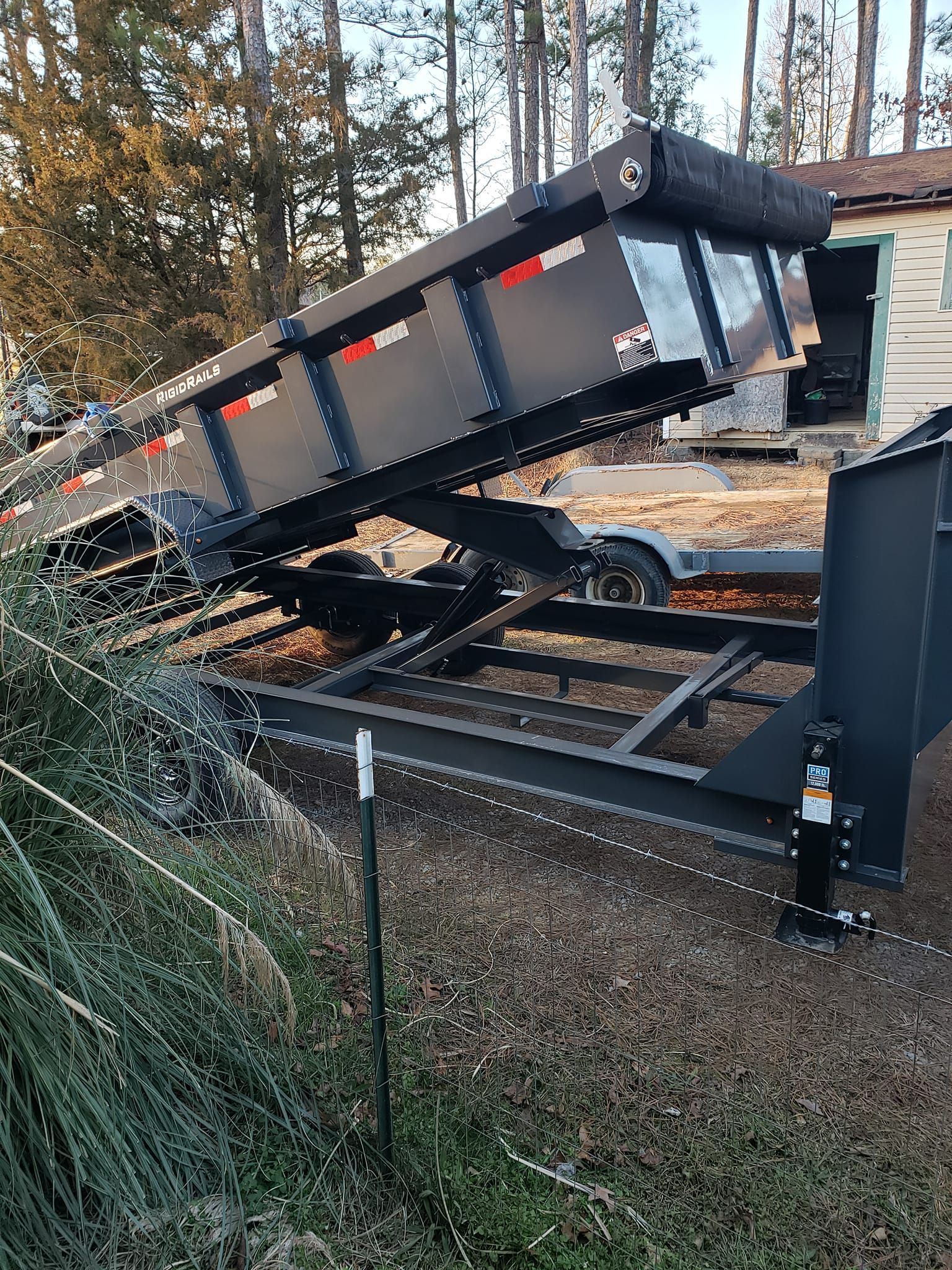 Overturned black dump truck on its side beside railroad tracks in a wooded area