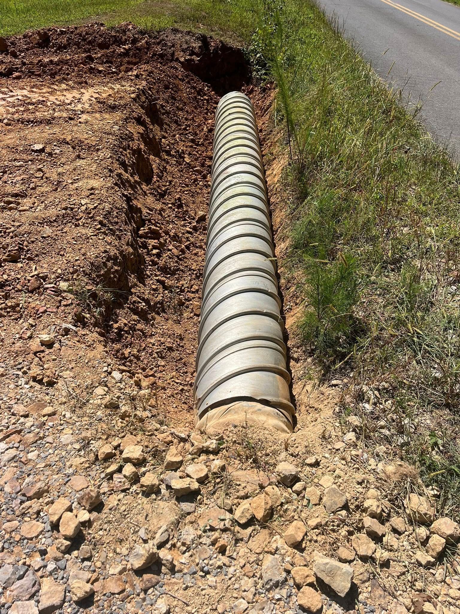 Corrugated drainage pipe running under a roadside ditch beside asphalt and gravel