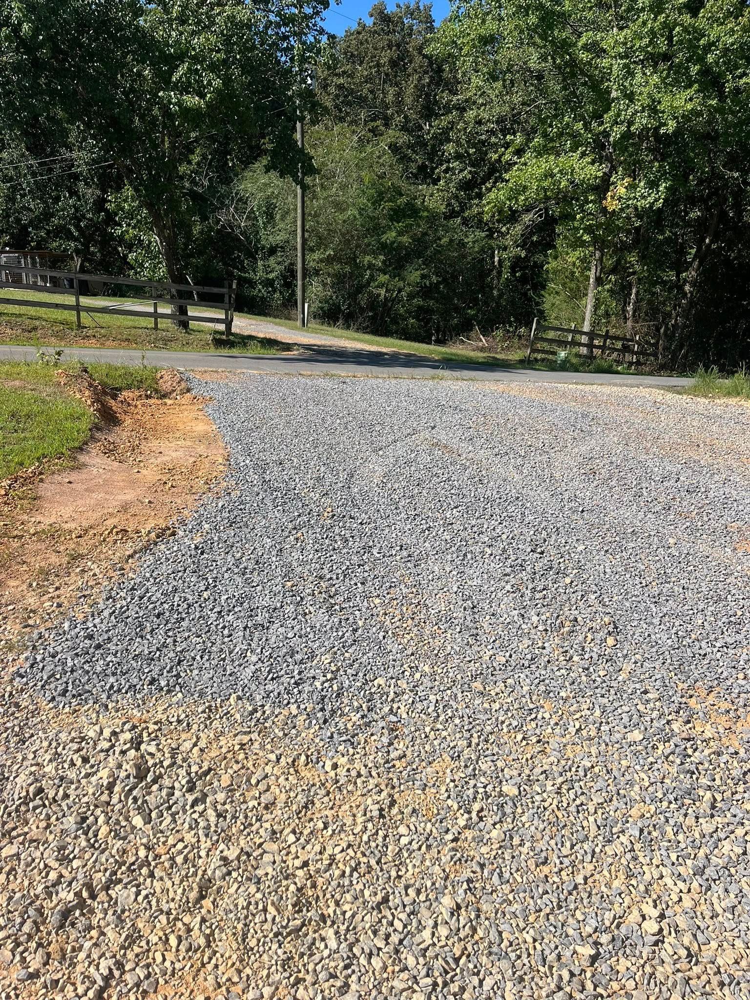 Gravel driveway curving through a wooded area with green trees and a dirt edge.