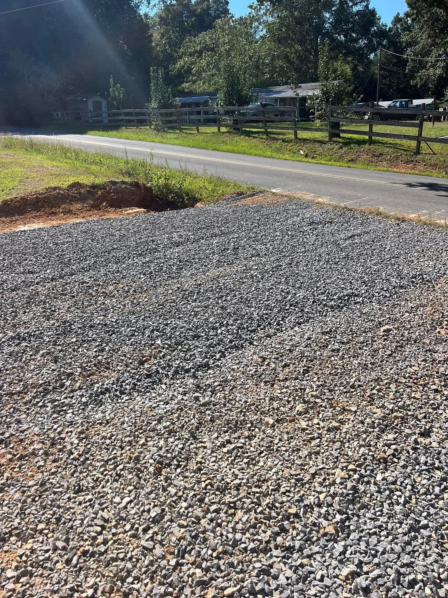 Gravel path beside a road with trees and parked cars in the background, lit by bright sunlight