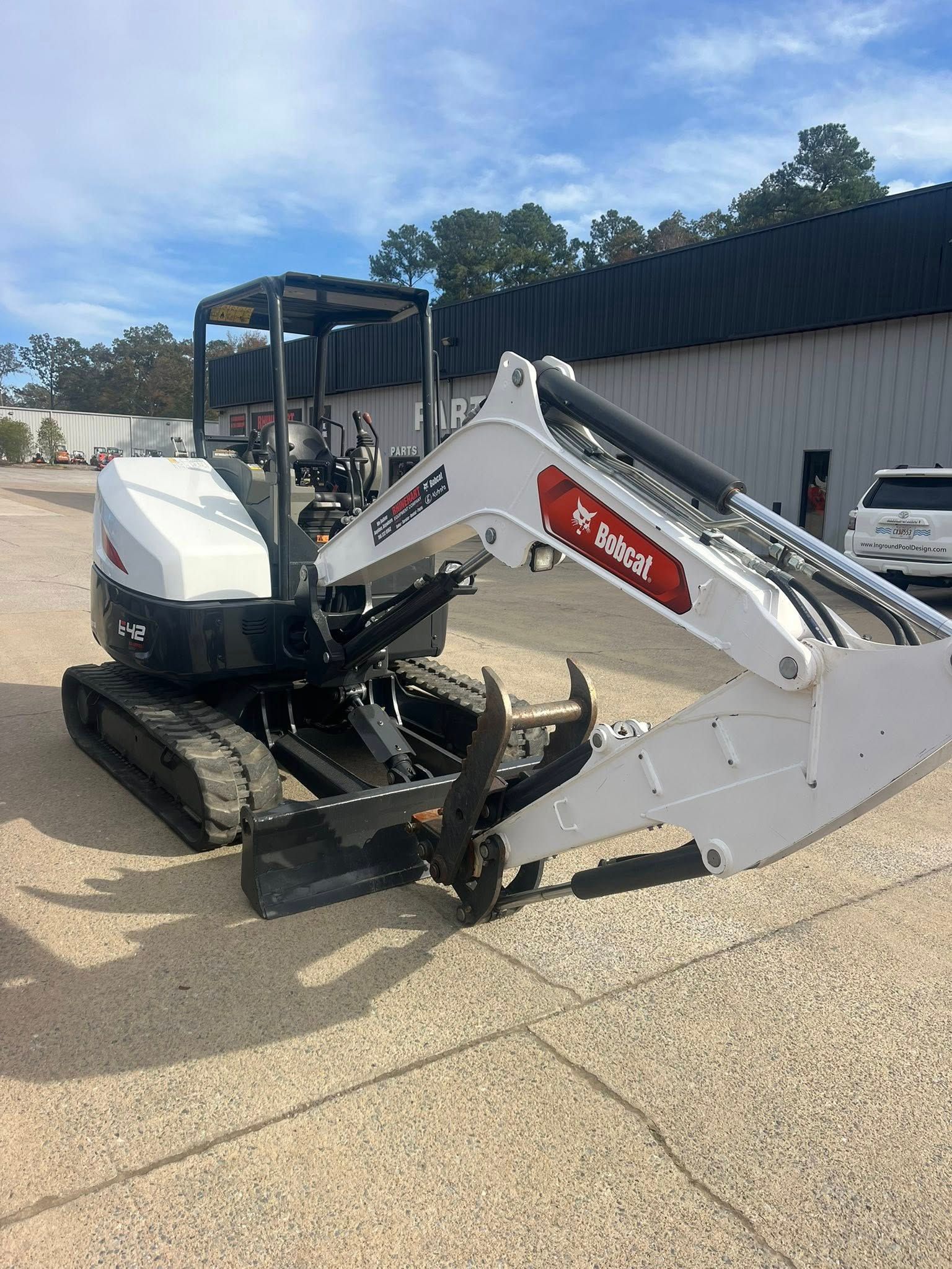White compact track loader with bucket and backhoe attachment parked outdoors near a building