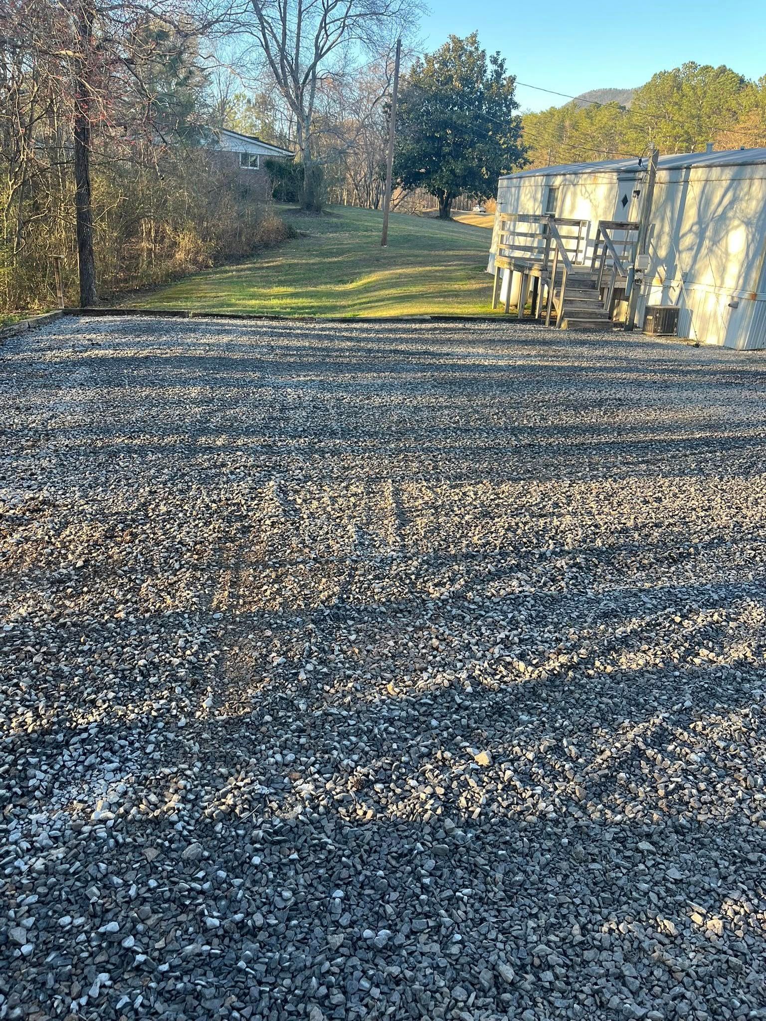 Gravel lot beside a long white building, with a grassy path and autumn trees in the background.