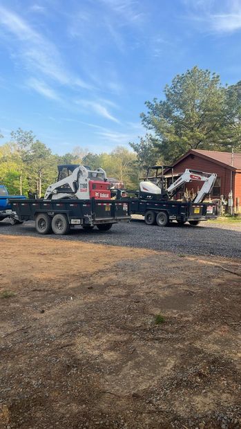 Two flatbed trucks hauling a small red cabin-like structure on a gravel lot under a blue sky