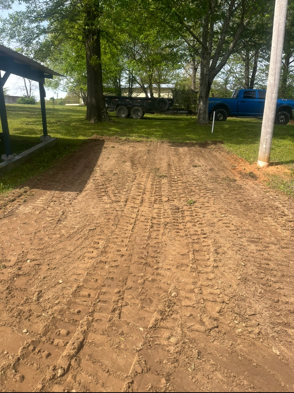 Dirt driveway between trees and a blue pickup truck in a rural yard