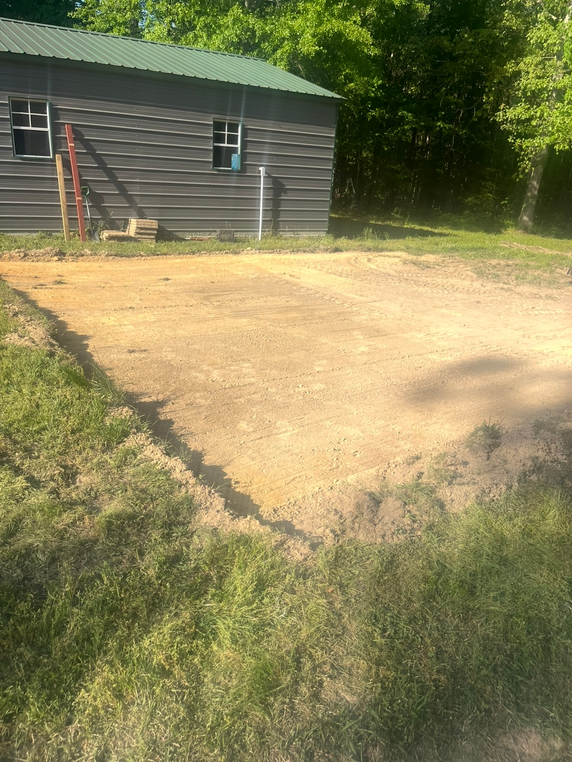 Gravel driveway beside a gray shed with a ladder leaning against it, bordered by grass and trees.