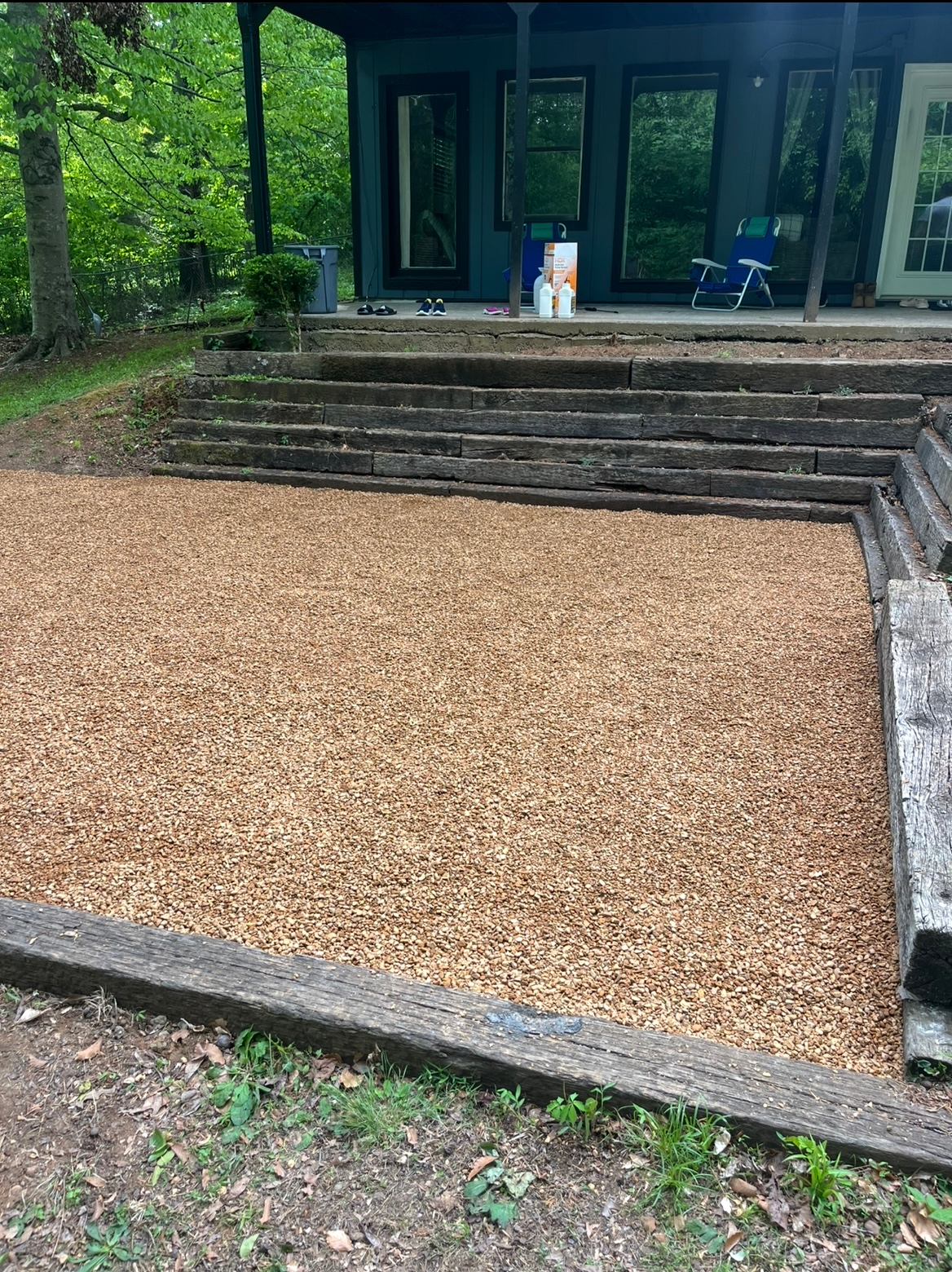 Gravel-covered courtyard beside concrete steps leading to a glass-front building, surrounded by trees.
