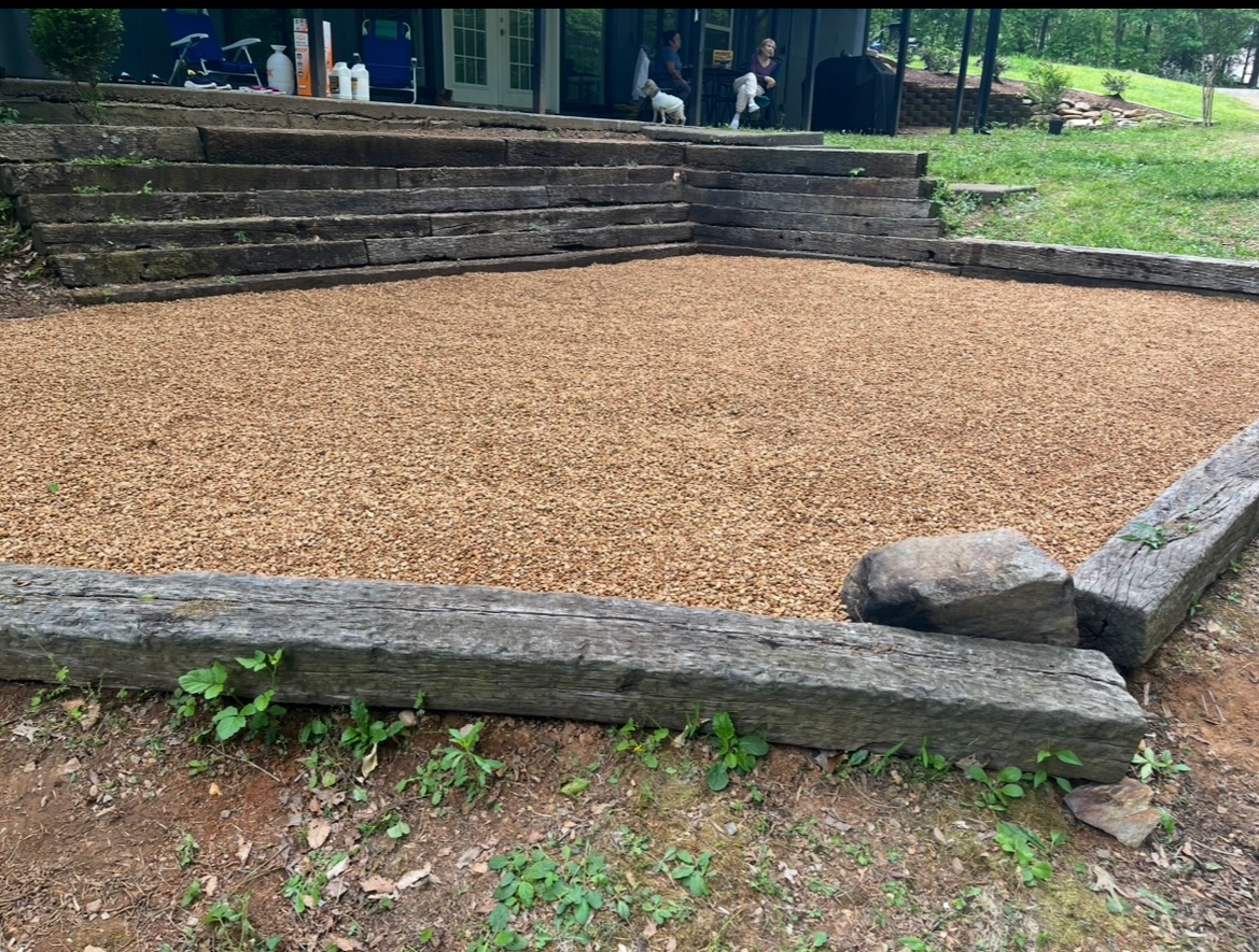 Outdoor gravel-filled stone-bordered area with steps and a large rock in a park-like setting