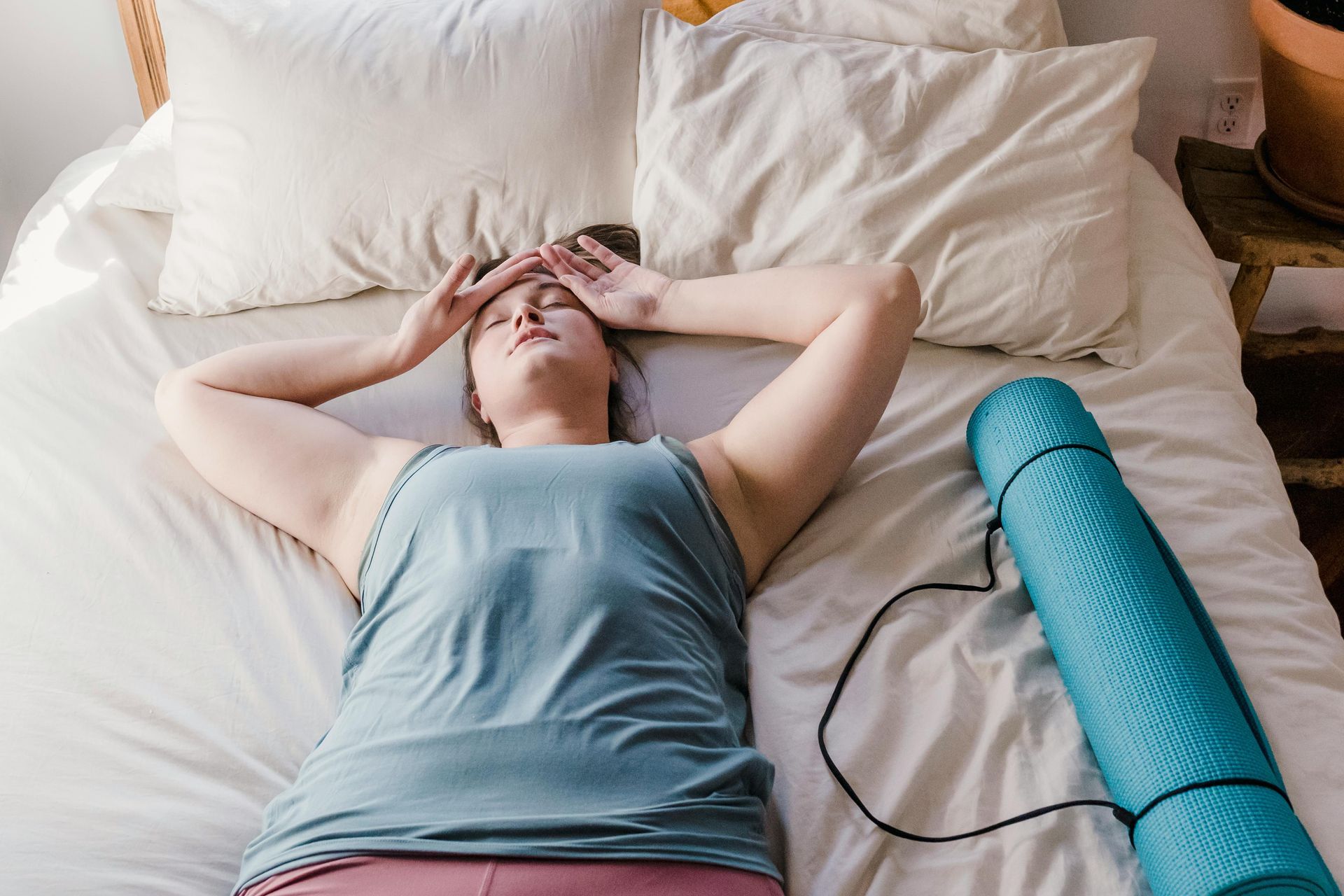 Person lying on a bed with hands over eyes beside a blue foam roller