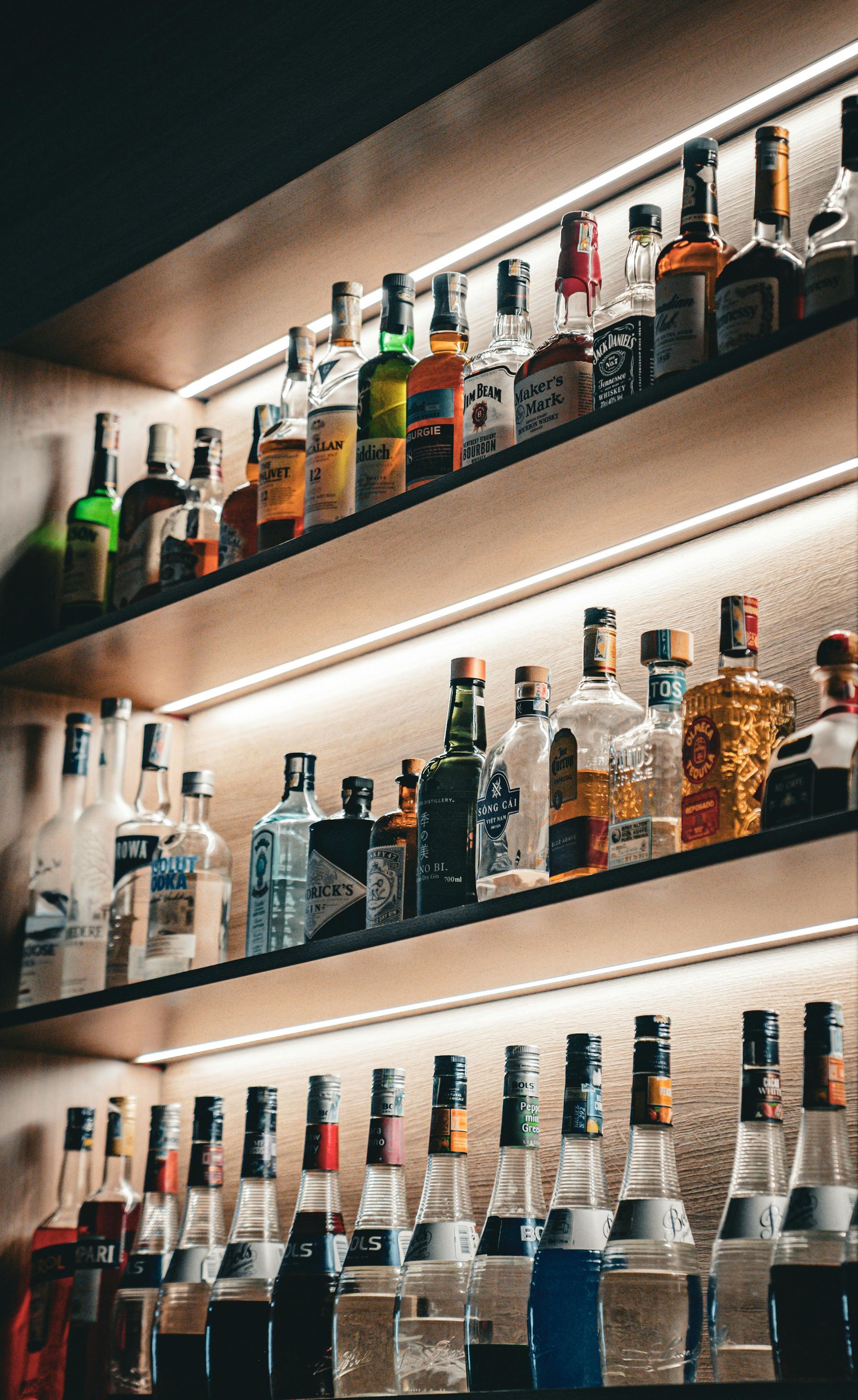 Rows of liquor bottles on illuminated bar shelves in a warm, dimly lit setting
