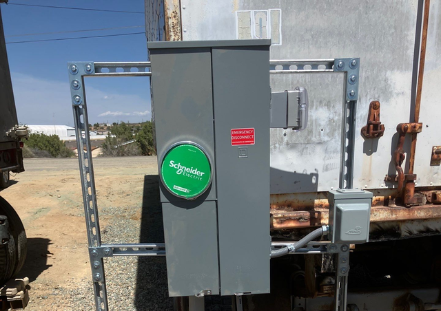Gray electrical control box with green sign mounted outdoors on industrial equipment.