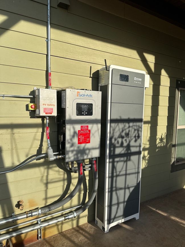 Electrical utility equipment mounted on a beige exterior wall, with gray panels and conduit pipes.