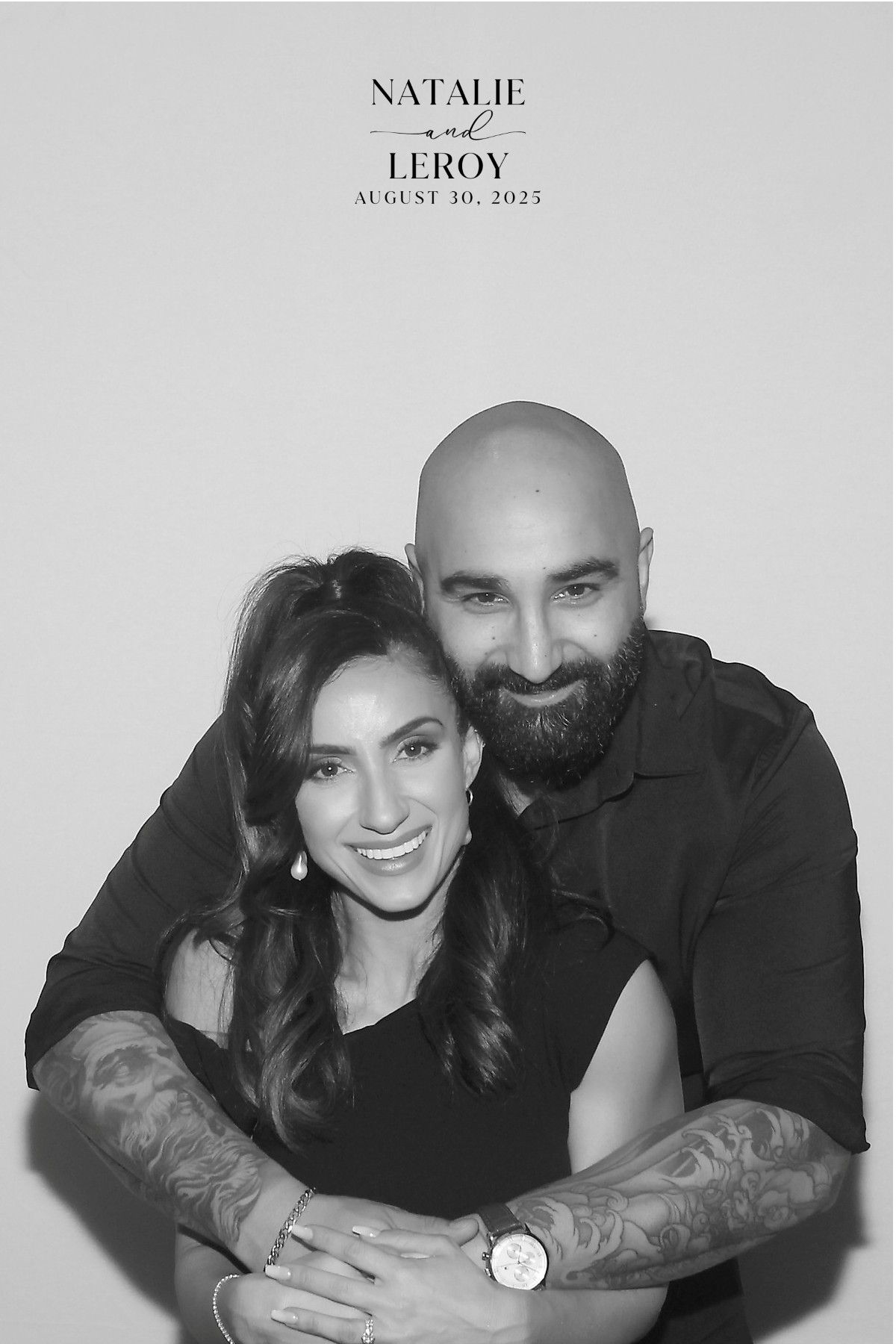 A black and white photo of a smiling couple hugging against a plain background, with their names and date printed above.