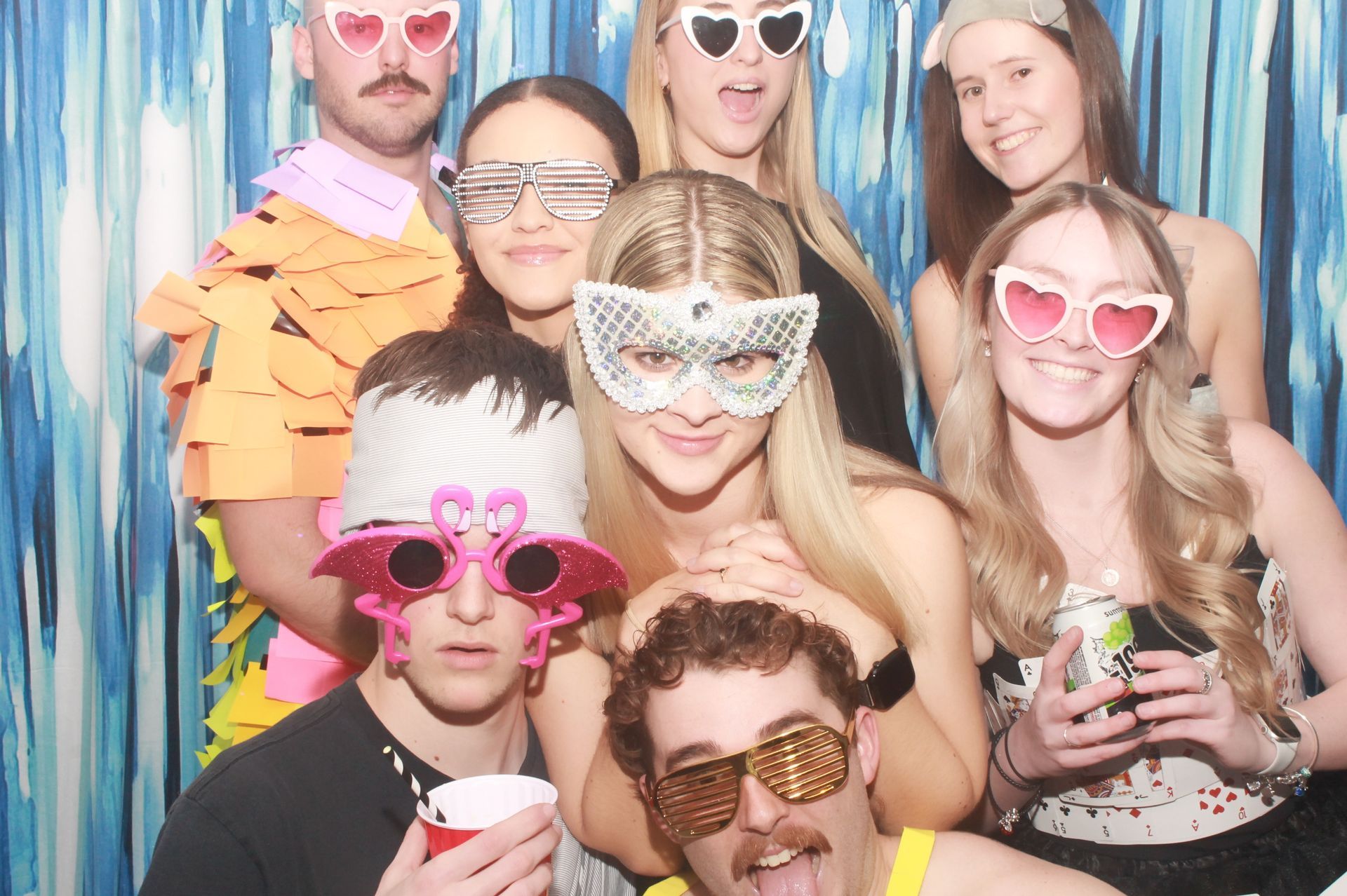 Group of people posing with fun photo booth props in front of a blue backdrop.