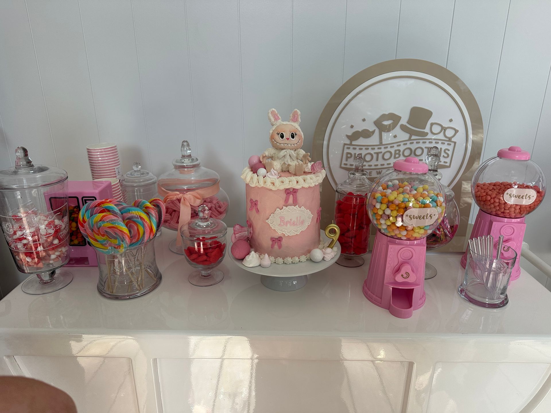 Candy table with cake topped with a bunny, candy jars, lollipops, and gumball machines.