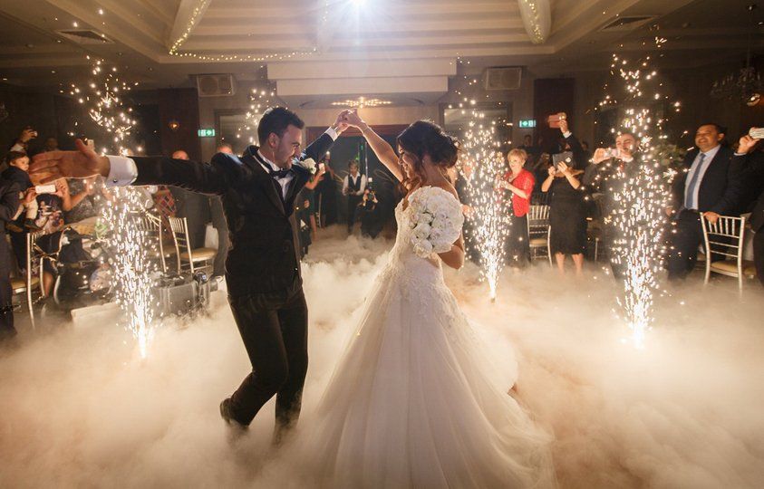 Bride and groom dance at wedding reception with pyrotechnics and fog.