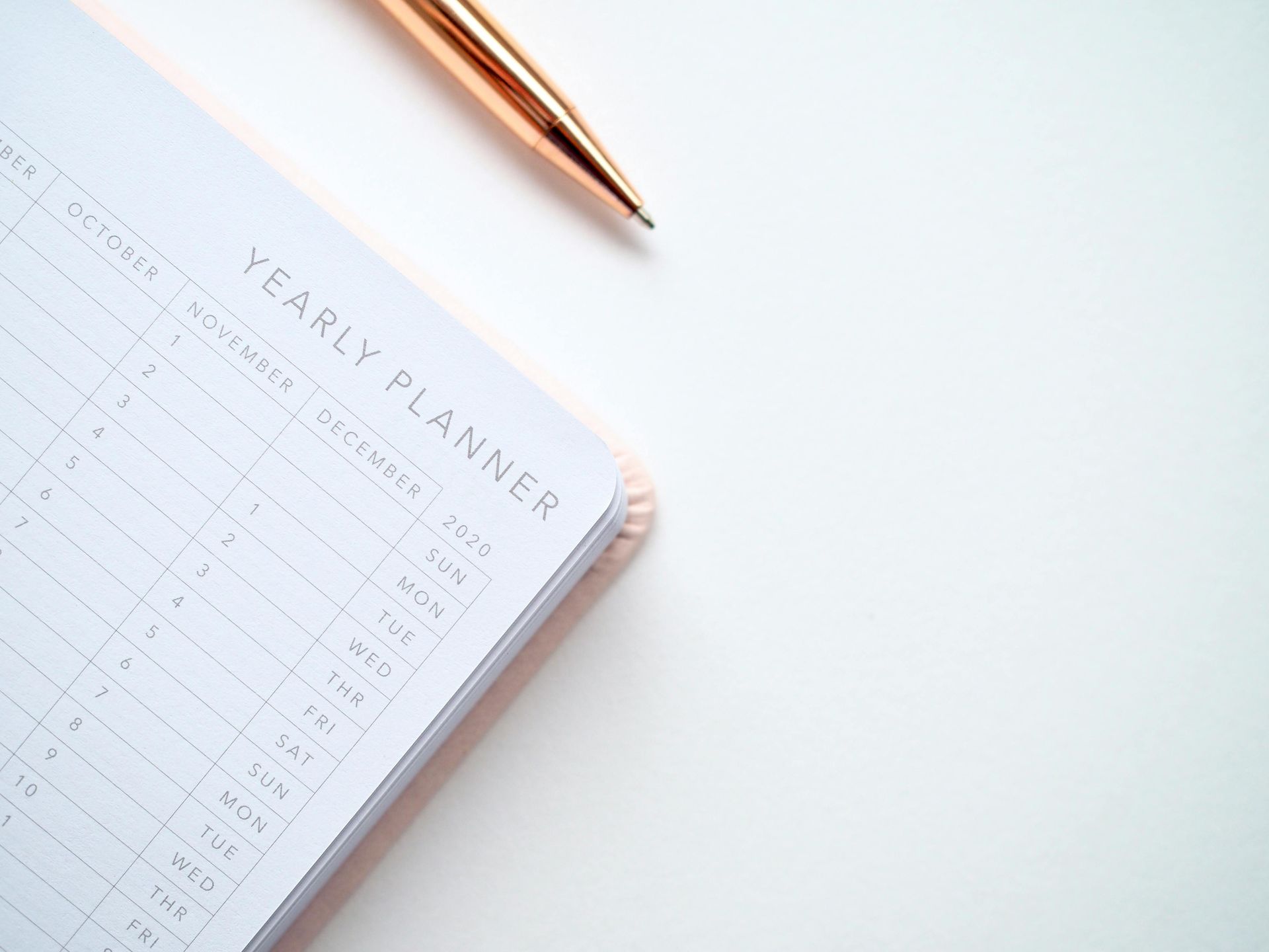A yearly planner is open next to a pen on a white surface.
