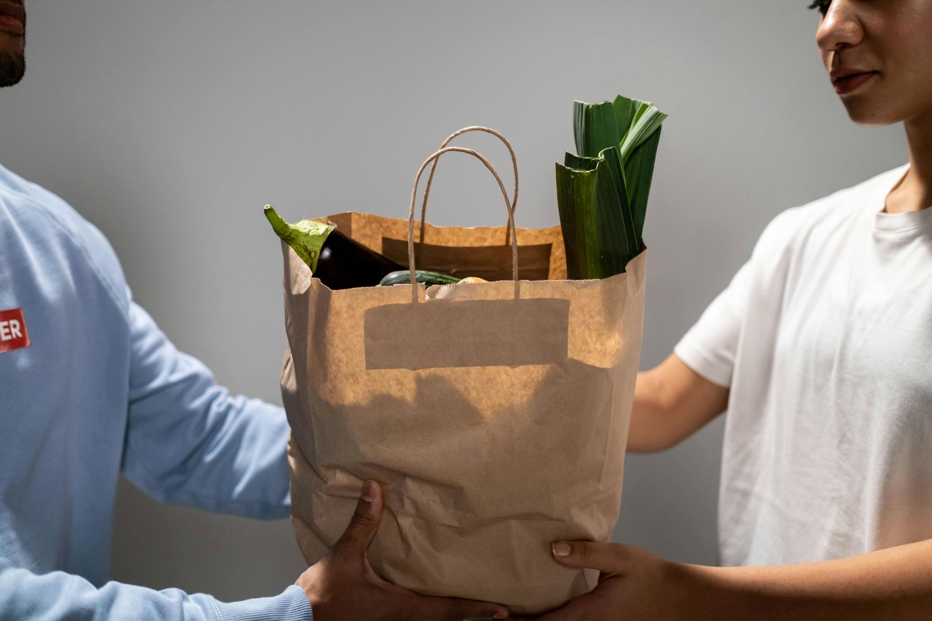 A man is handing a bag of vegetables to a woman.