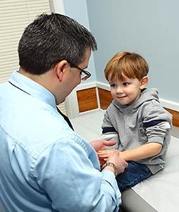 Doctor examining a young boy's hand in a medical setting. Both are smiling.
