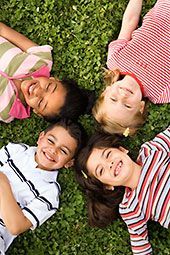 Four diverse children smiling, lying on green grass, looking upwards.