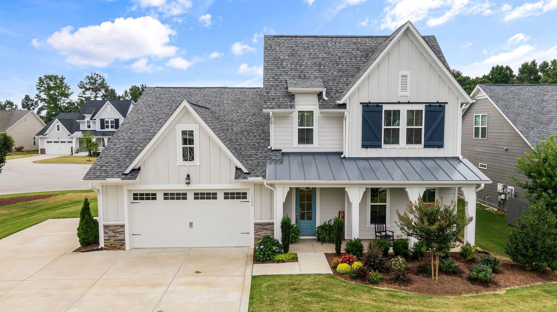 Two-story gray house with white trim, front porch, and attached garage in a suburban neighborhood.