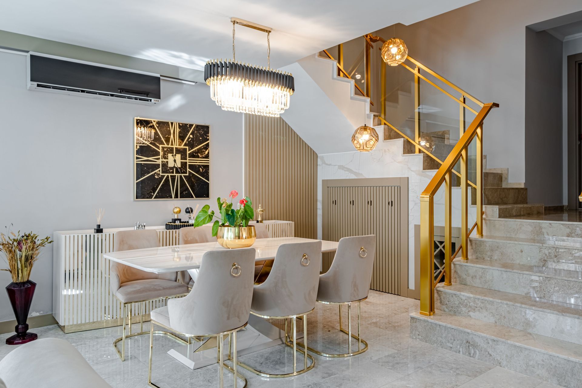 Modern dining room with white chairs, gold accents, chandelier, staircase, and marble tile floor