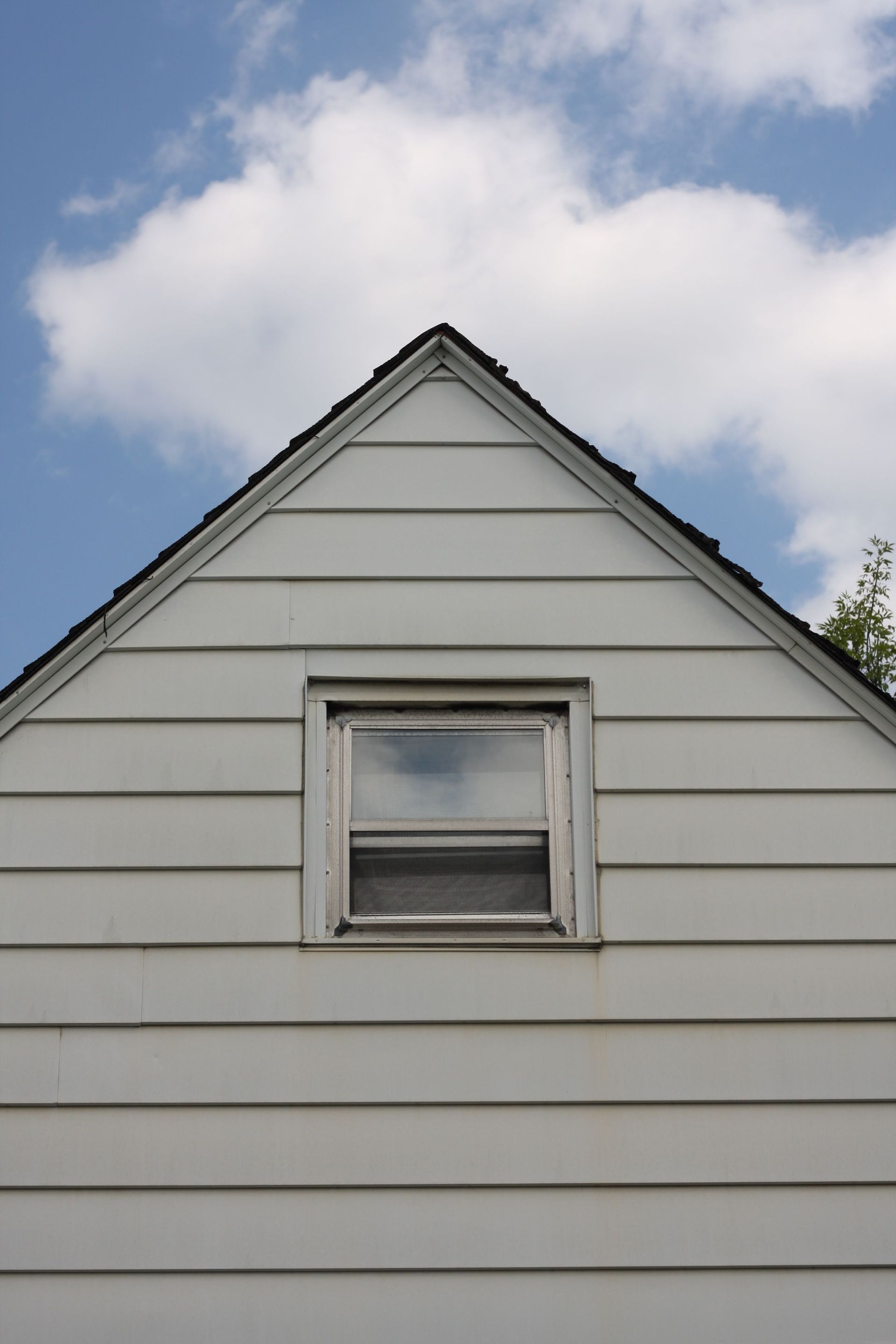 White house gable with a small window against a partly cloudy blue sky