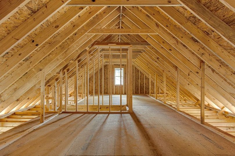 Interior of an unfinished wooden attic with exposed roof framing and a small window at the far end.