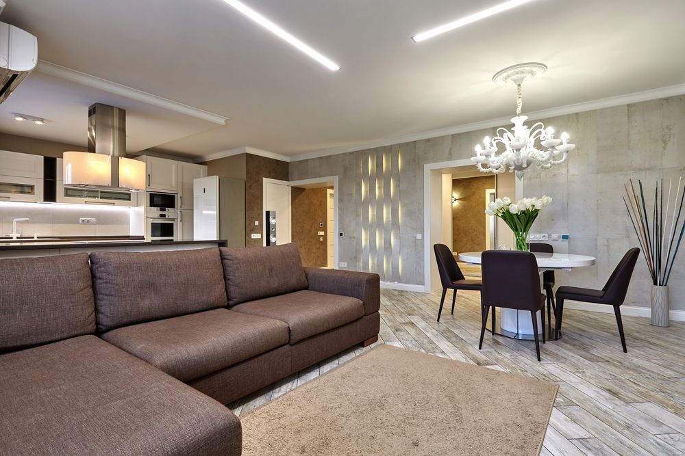 Modern open-plan living room with brown sectional sofa, dining table, and chandelier in a gray-toned interior